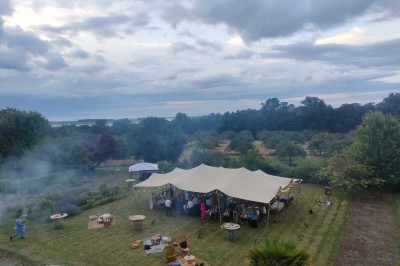 Table en bois rustique dressée pour un repas, avec vaisselle fleurie, bougies, rondins de bois et chemin de table vert.