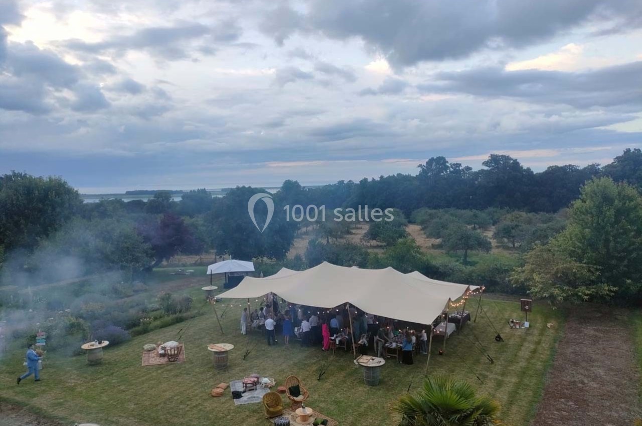 Tente blanche abritant un rassemblement en plein air dans un jardin verdoyant sous un ciel nuageux.