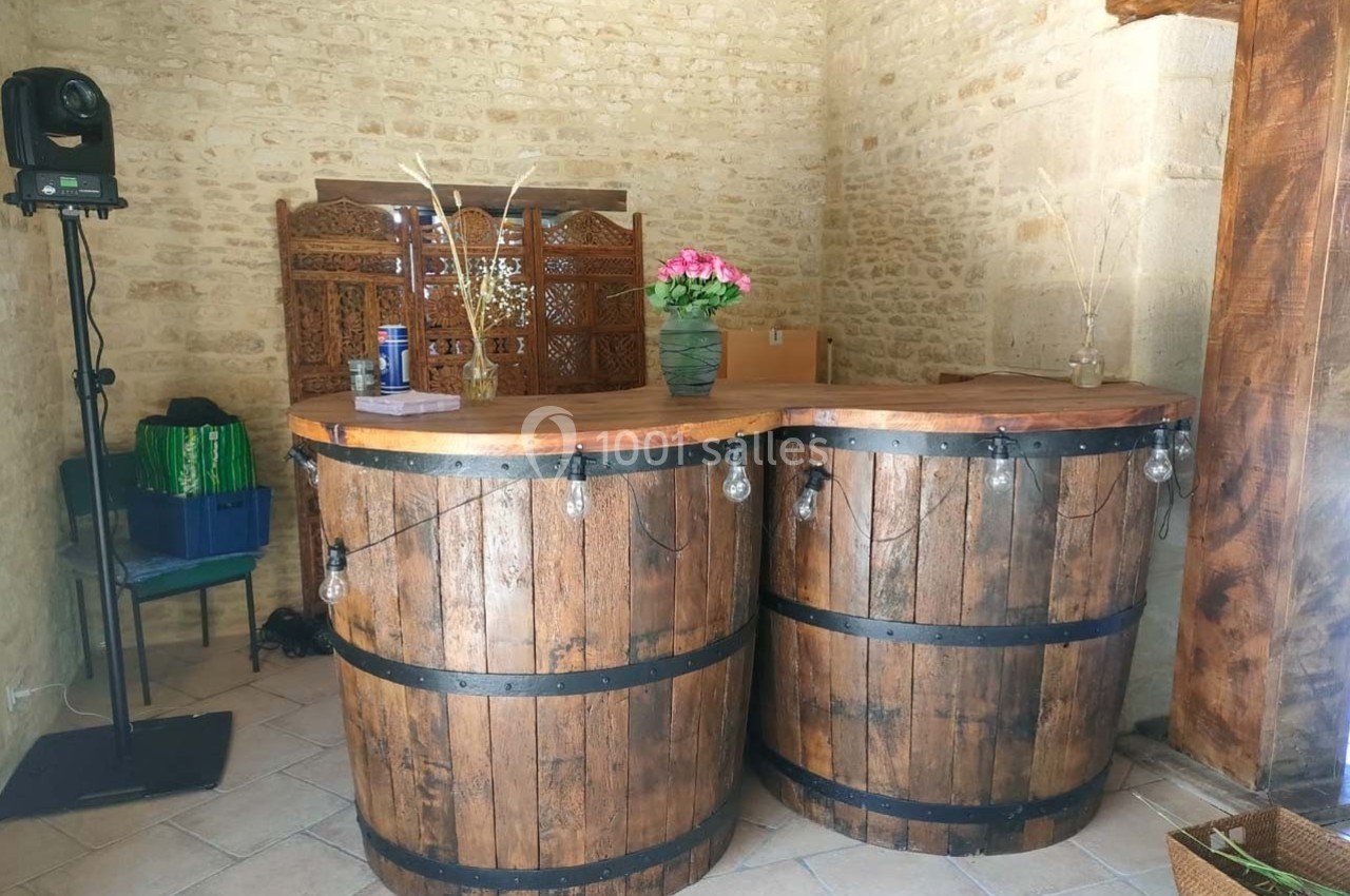 Comptoir en bois fabriqué à partir de tonneaux, décoré de guirlandes lumineuses, dans une pièce en pierre.