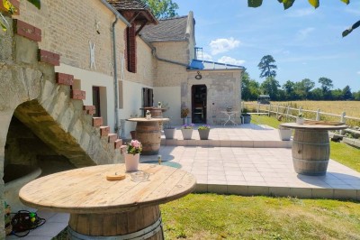 Table en bois rustique dressée pour un repas, avec vaisselle fleurie, bougies, rondins de bois et chemin de table vert.