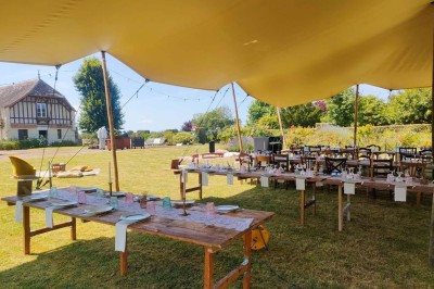 Table en bois rustique dressée pour un repas, avec vaisselle fleurie, bougies, rondins de bois et chemin de table vert.
