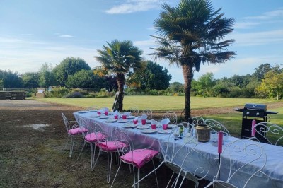 Table en bois rustique dressée pour un repas, avec vaisselle fleurie, bougies, rondins de bois et chemin de table vert.