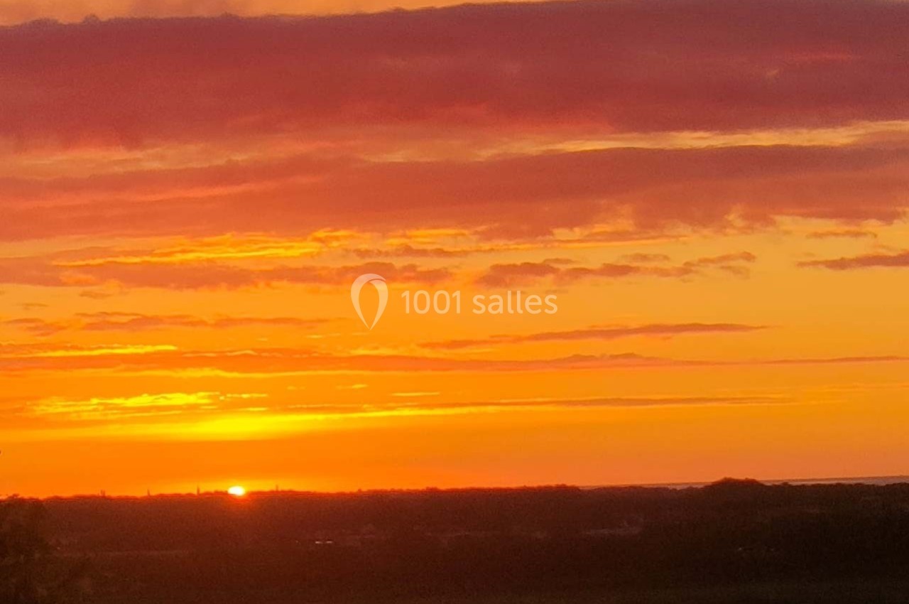 Coucher de soleil avec un ciel aux teintes orange et rose, illuminant un paysage sombre à l'horizon.