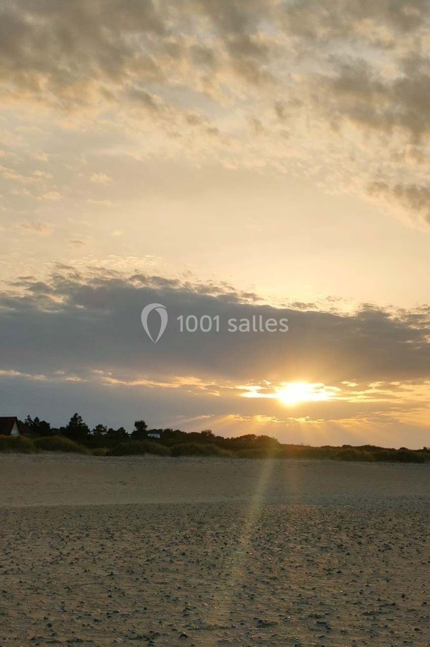 Plage déserte au coucher du soleil avec un ciel partiellement nuageux et des dunes en arrière-plan.