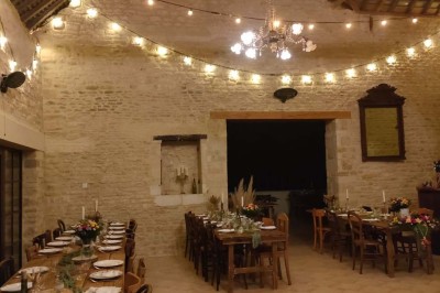 Table en bois rustique dressée pour un repas, avec vaisselle fleurie, bougies, rondins de bois et chemin de table vert.