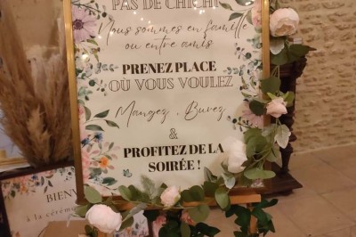 Table en bois rustique dressée pour un repas, avec vaisselle fleurie, bougies, rondins de bois et chemin de table vert.