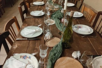 Table en bois rustique dressée pour un repas, avec vaisselle fleurie, bougies, rondins de bois et chemin de table vert.