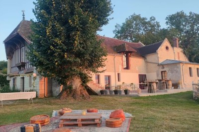 Table en bois rustique dressée pour un repas, avec vaisselle fleurie, bougies, rondins de bois et chemin de table vert.
