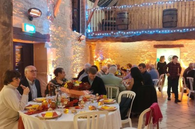 Table en bois rustique dressée pour un repas, avec vaisselle fleurie, bougies, rondins de bois et chemin de table vert.