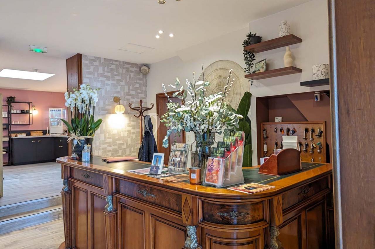 Comptoir en bois ancien décoré de fleurs, situé dans un espace intérieur lumineux avec des étagères et un mur texturé.