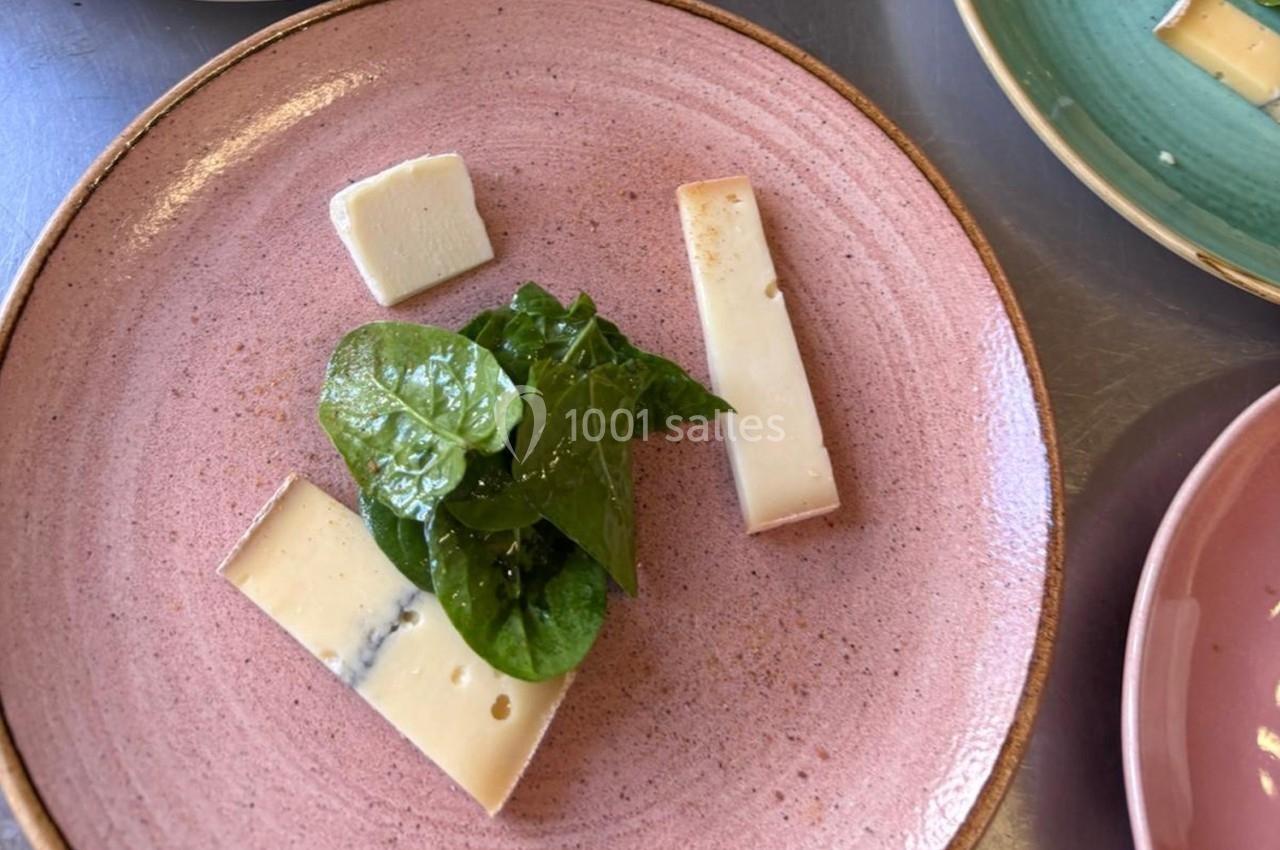 Assiette rose contenant des morceaux de fromage et quelques feuilles de salade verte fraîche.
