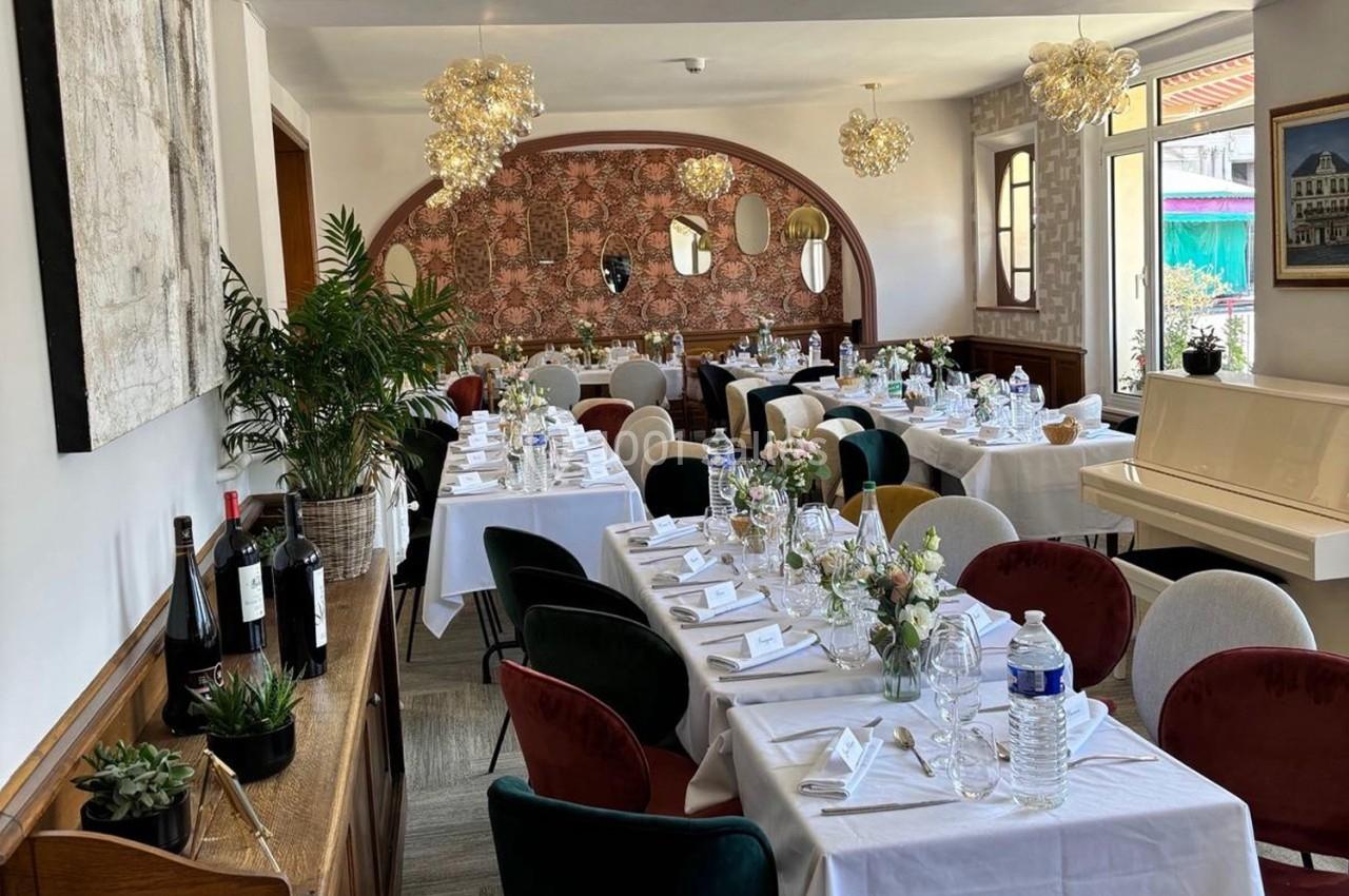 Salle de restaurant élégamment décorée avec des tables dressées, des chaises colorées et des luminaires suspendus.
