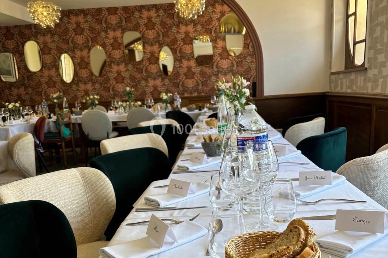 Salle de réception élégante avec tables dressées, nappes blanches, vaisselle, fleurs et miroirs décoratifs au mur.