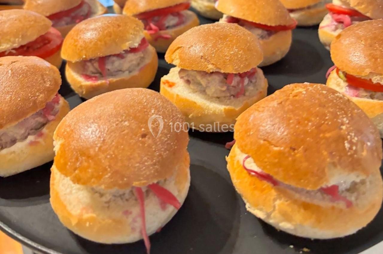 Petits burgers garnis de viande hachée, tranches de tomate et crudités, disposés sur un plateau noir.