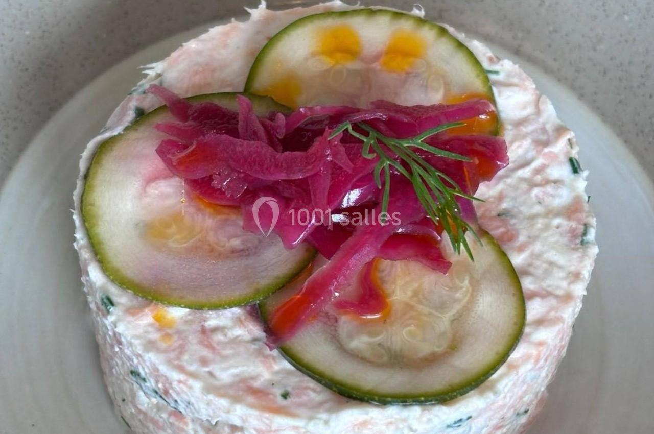 Terrine de poisson garnie de rondelles de concombre, oignons rouges marinés et brin d'aneth sur une assiette blanche.
