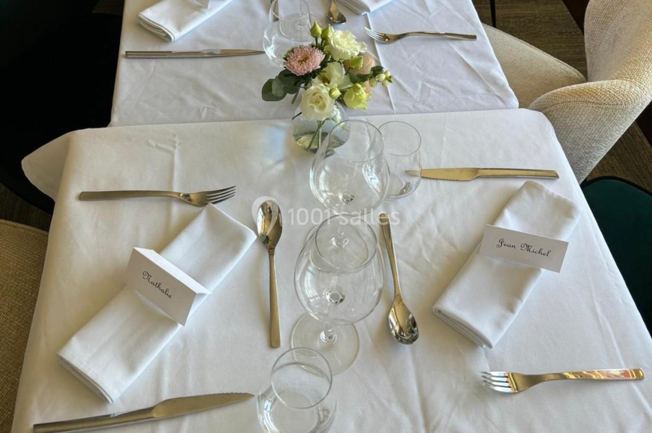 Table dressée avec nappe blanche, couverts, verres, serviettes pliées et un centre de table floral.
