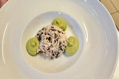 Une assiette contenant une préparation de poisson effiloché avec des herbes, accompagnée de trois points de purée verte.