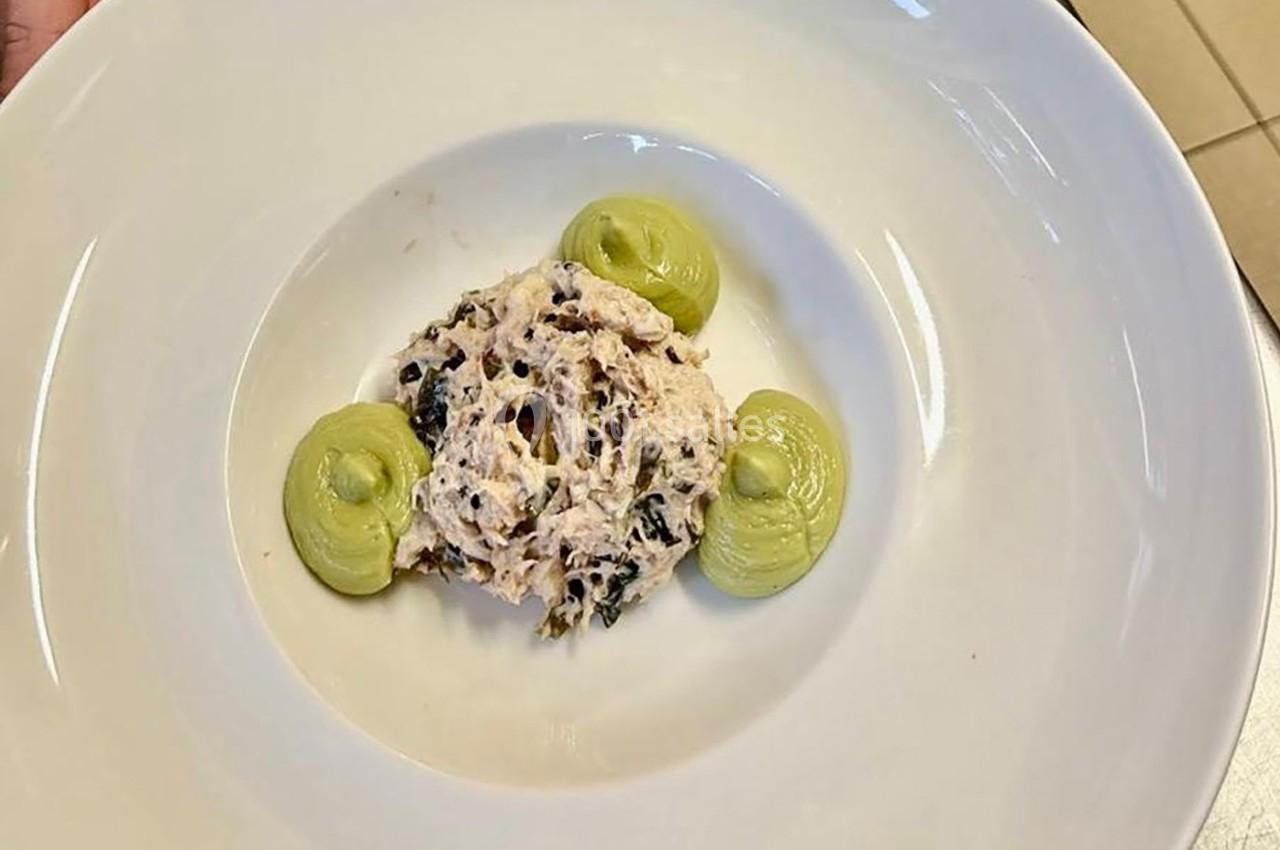 Une assiette contenant une préparation de poisson effiloché avec des herbes, accompagnée de trois points de purée verte.