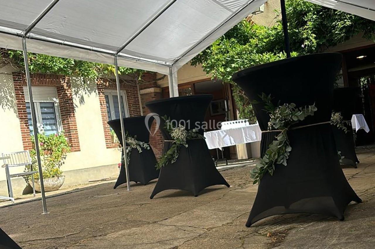 Tables hautes noires décorées de feuillages sous une tente blanche dans une cour pavée.