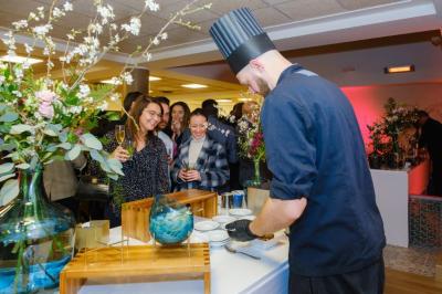 Salle décorée avec des ballons roses, éclairage violet, deux personnes marchant au centre, tables hautes et chaises…