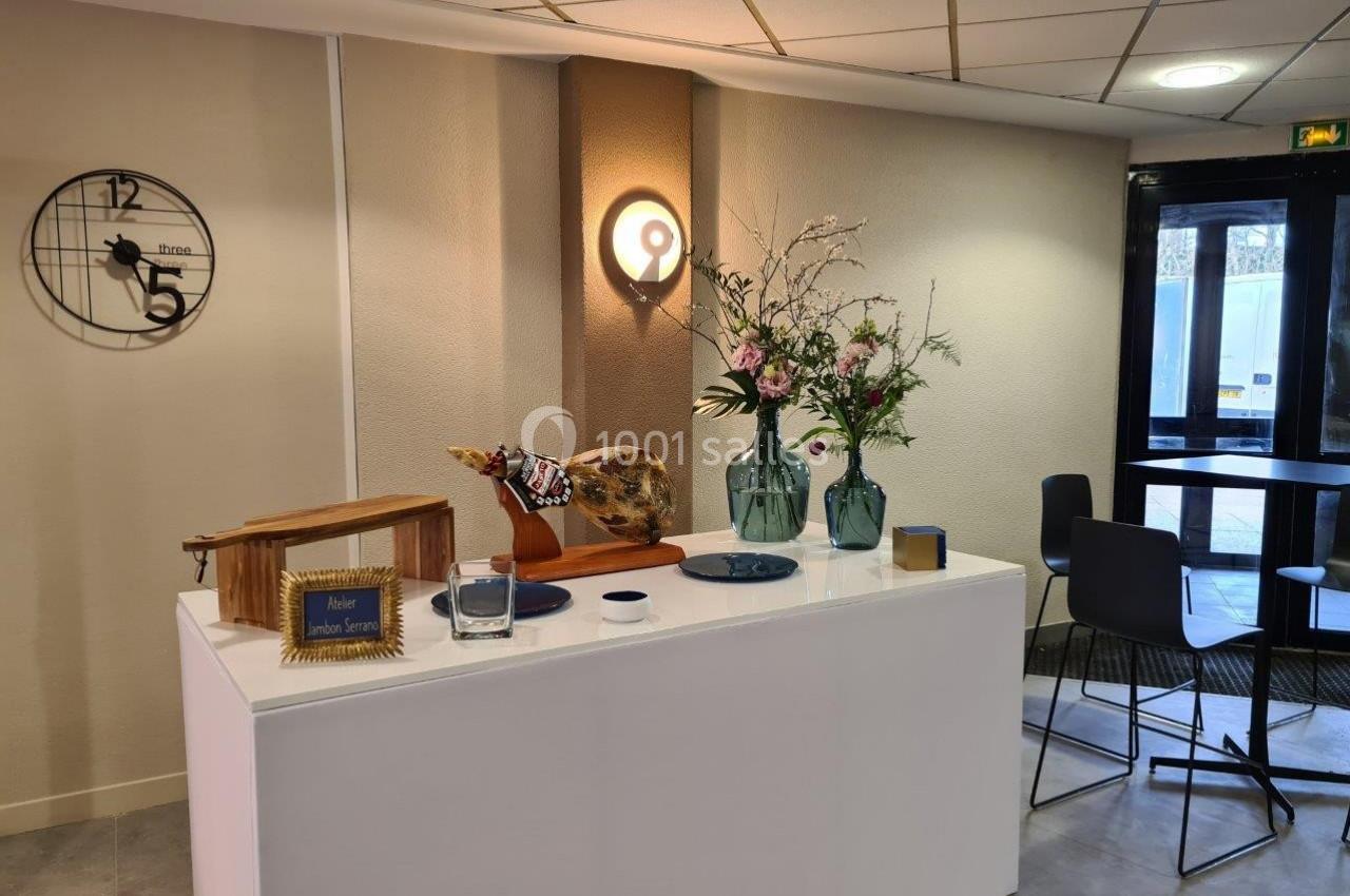 Comptoir avec décoration florale, horloge murale, jambon sur support et chaises près d'une porte vitrée.