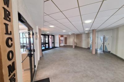 Salle décorée avec des ballons roses, éclairage violet, deux personnes marchant au centre, tables hautes et chaises…