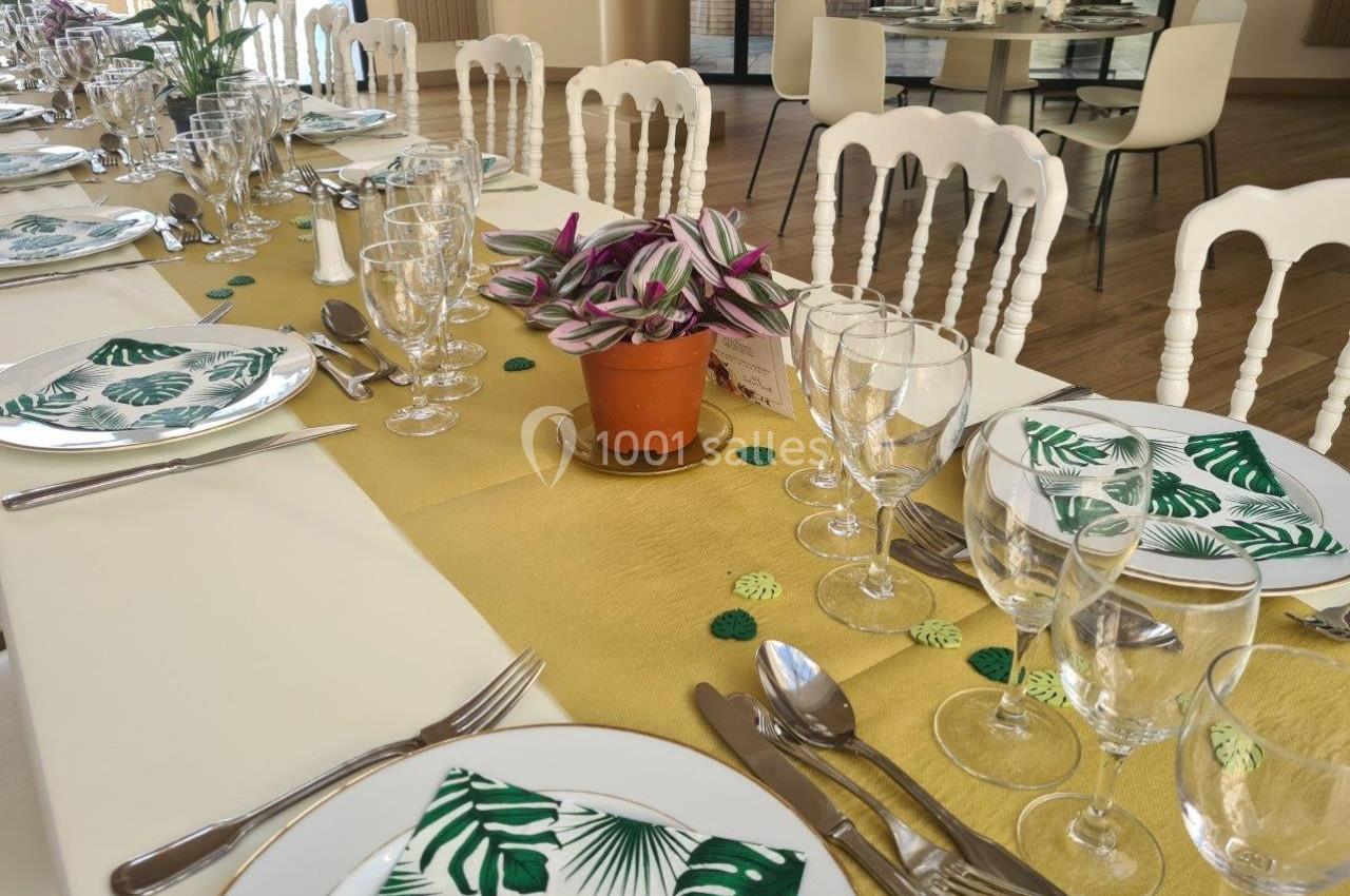 Table dressée avec une nappe dorée, vaisselle élégante, serviettes à motif végétal et plante en pot comme centre de table.