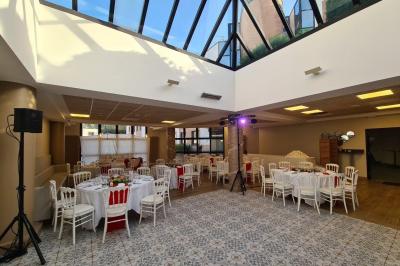 Salle décorée avec des ballons roses, éclairage violet, deux personnes marchant au centre, tables hautes et chaises…