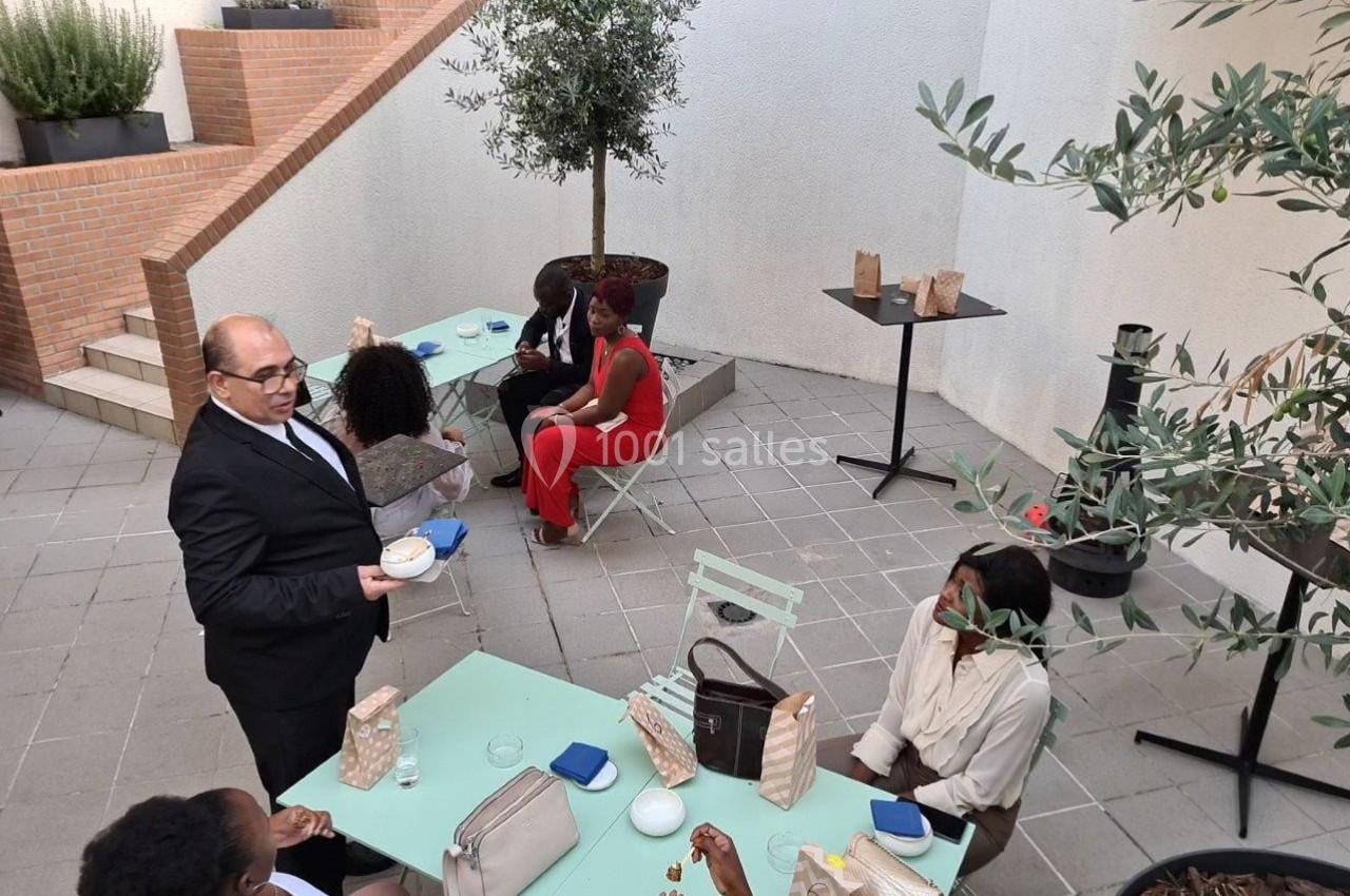 Un groupe de personnes discute et partage un moment convivial sur une terrasse aménagée avec tables et plantes.