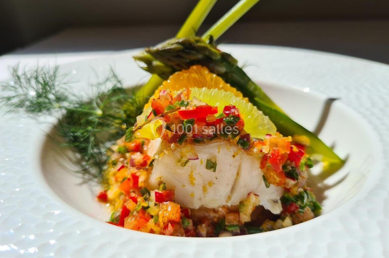 Filet de poisson garni de légumes colorés et d'herbes fraîches, accompagné d'asperges et de tranches d'orange.