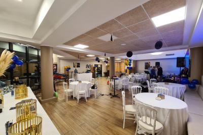 Salle décorée avec des ballons roses, éclairage violet, deux personnes marchant au centre, tables hautes et chaises…