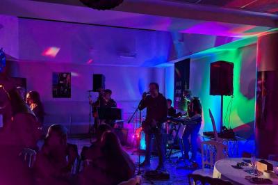 Salle décorée avec des ballons roses, éclairage violet, deux personnes marchant au centre, tables hautes et chaises…