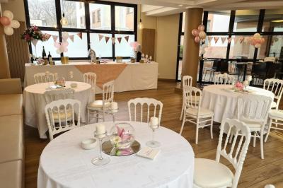 Salle décorée avec des ballons roses, éclairage violet, deux personnes marchant au centre, tables hautes et chaises…