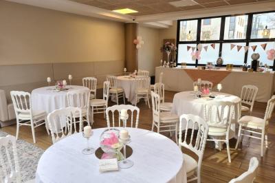 Salle décorée avec des ballons roses, éclairage violet, deux personnes marchant au centre, tables hautes et chaises…