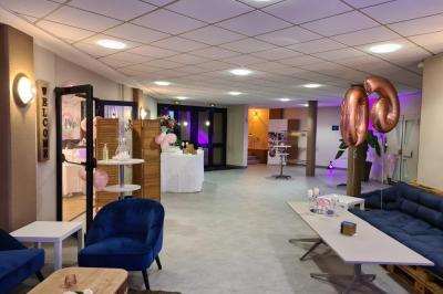 Salle décorée avec des ballons roses, éclairage violet, deux personnes marchant au centre, tables hautes et chaises…