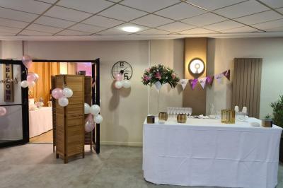 Salle décorée avec des ballons roses, éclairage violet, deux personnes marchant au centre, tables hautes et chaises…