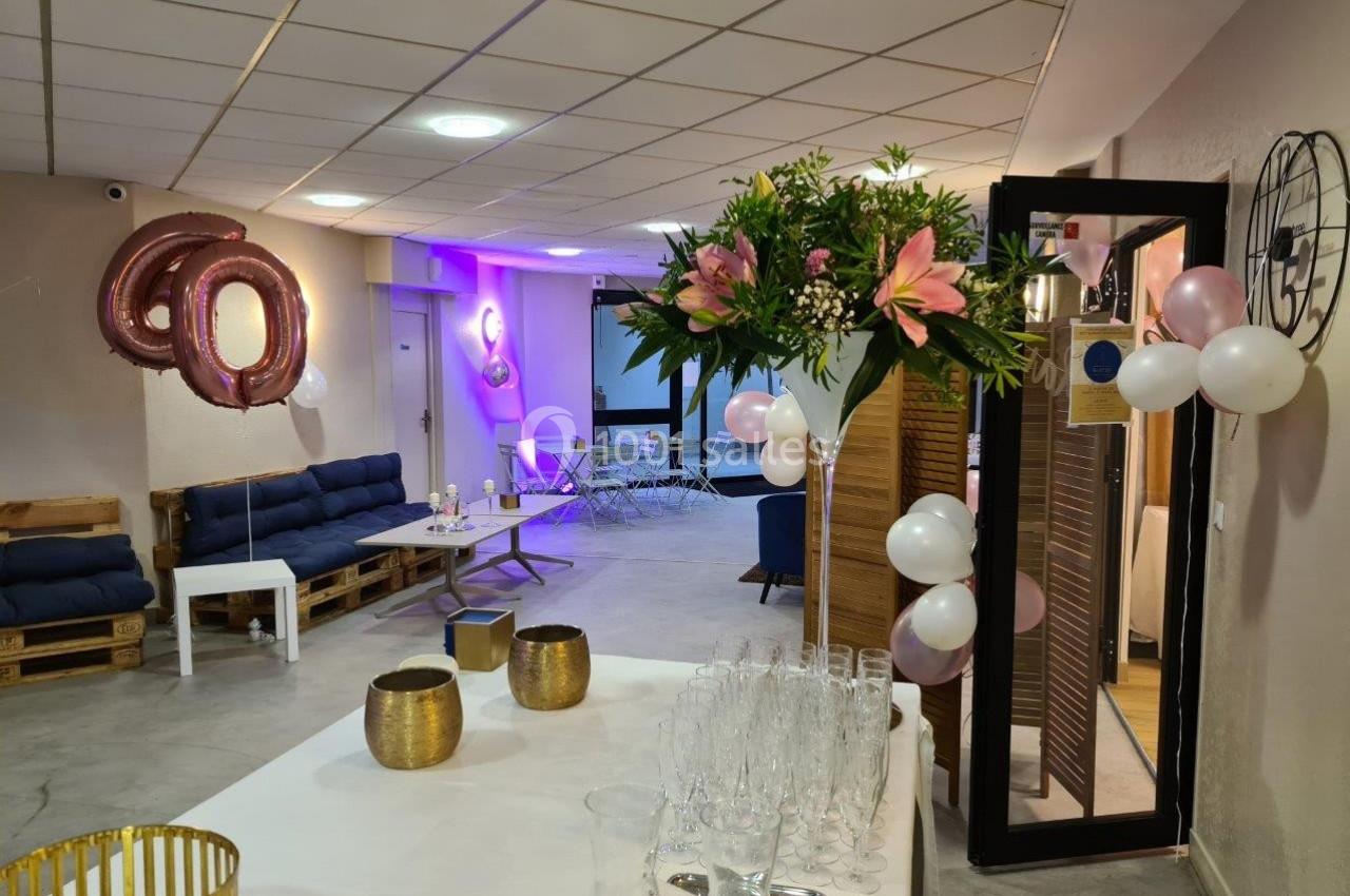 Salle décorée pour une fête avec ballons, fleurs, tables dressées et canapés en palettes.