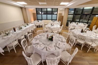 Salle décorée avec des ballons roses, éclairage violet, deux personnes marchant au centre, tables hautes et chaises…
