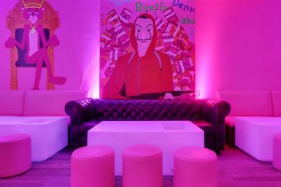 Salle de bar aux murs roses avec banquettes blanches, tabourets assortis et néons décoratifs.