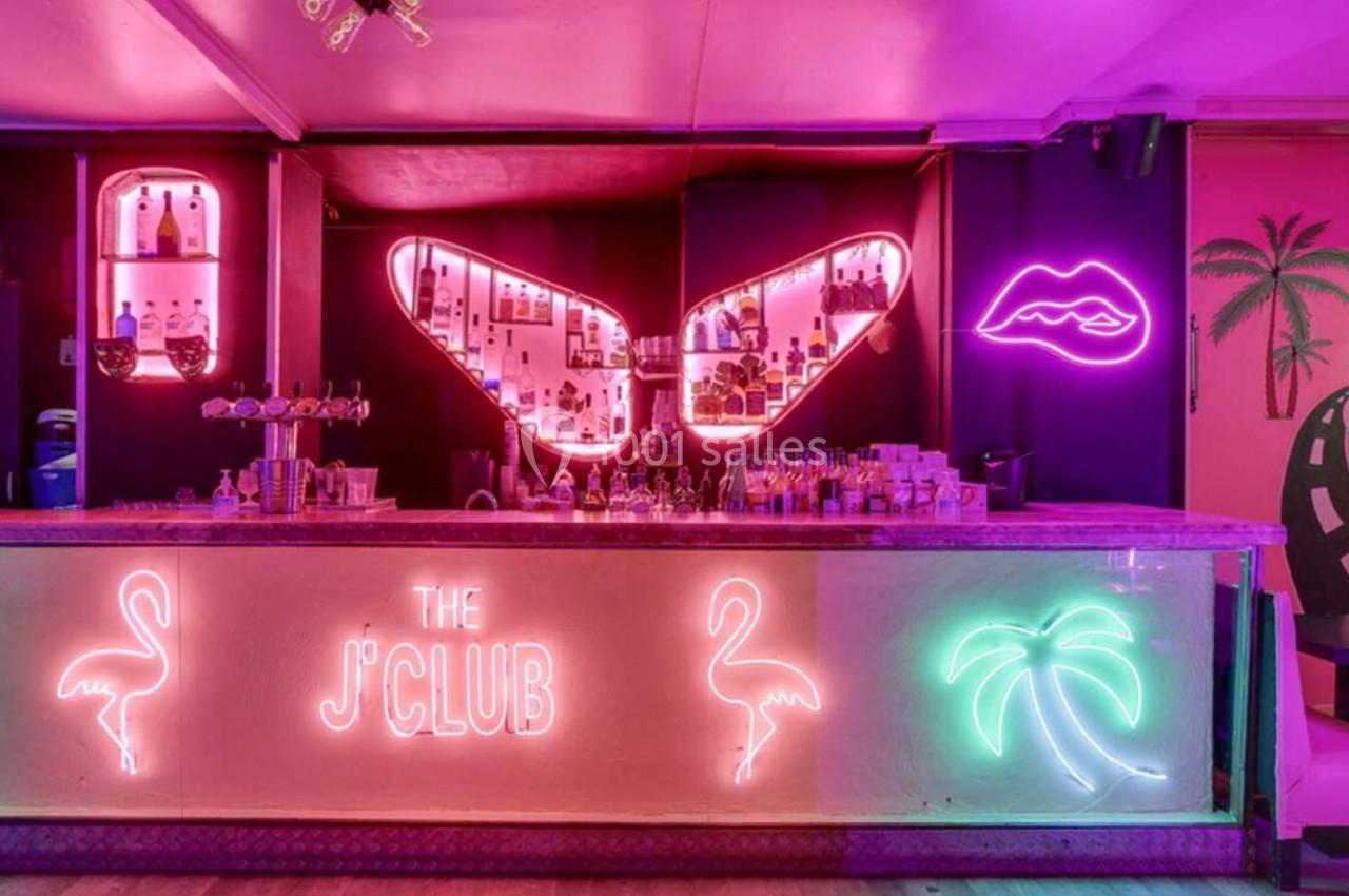 Bar avec comptoir éclairé par des néons colorés représentant des flamants roses, un palmier et des motifs lumineux.