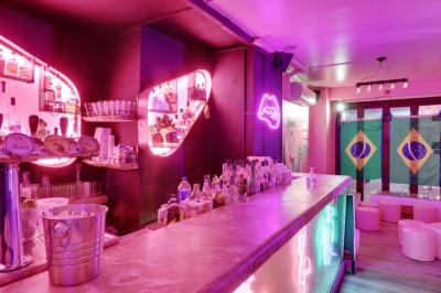 Salle de bar aux murs roses avec banquettes blanches, tabourets assortis et néons décoratifs.