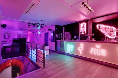Salle de bar aux murs roses avec banquettes blanches, tabourets assortis et néons décoratifs.