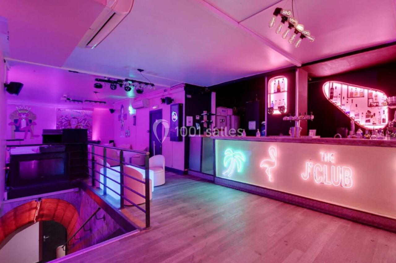 Intérieur d'un bar avec éclairage néon rose et violet, comptoir lumineux et décorations tropicales.