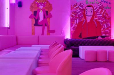 Salle de bar aux murs roses avec banquettes blanches, tabourets assortis et néons décoratifs.