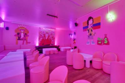 Salle de bar aux murs roses avec banquettes blanches, tabourets assortis et néons décoratifs.