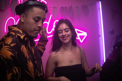 Salle de bar aux murs roses avec banquettes blanches, tabourets assortis et néons décoratifs.