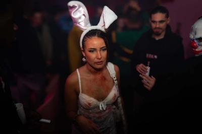 Salle de bar aux murs roses avec banquettes blanches, tabourets assortis et néons décoratifs.