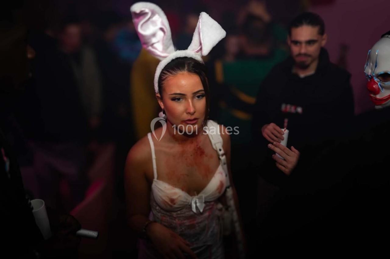 Une femme déguisée en lapin ensanglanté dans une ambiance de fête sombre avec des personnes en arrière-plan.
