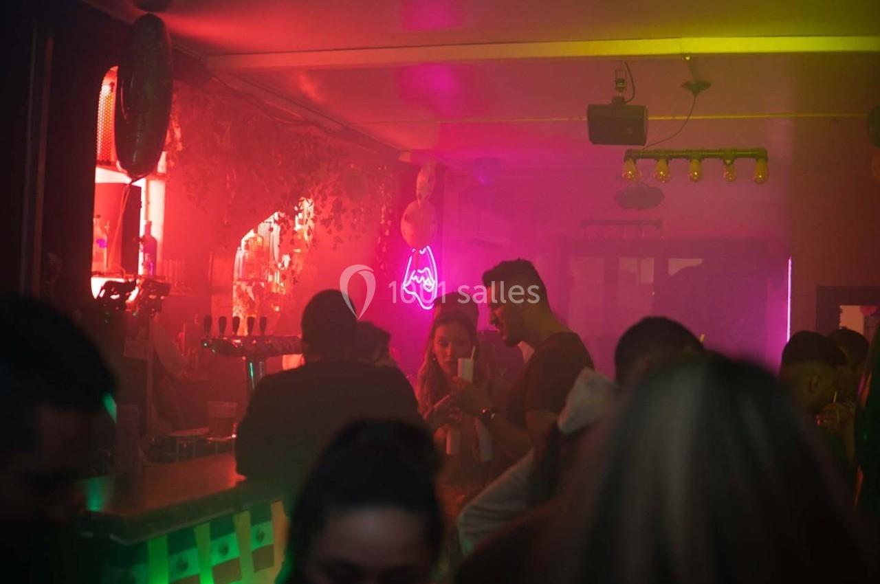 Personnes discutant dans un bar à l'éclairage tamisé avec des néons colorés et une ambiance festive.