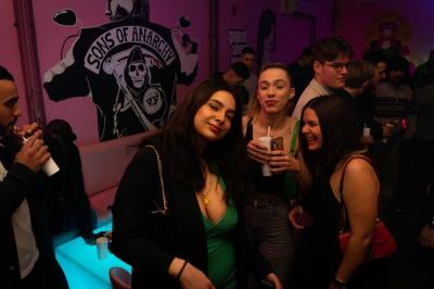Salle de bar aux murs roses avec banquettes blanches, tabourets assortis et néons décoratifs.